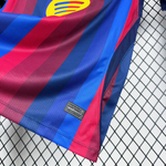 Close-up of a striped FC Barcelona soccer jersey showing the blue and red stripes, a yellow club crest, and a black manufacturer label on a white mesh background.