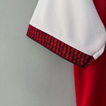 Close-up of a white athletic sleeve with a red and black geometric patterned cuff trim, shown against a light gray background.
