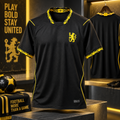 A black short-sleeve soccer jersey with yellow trim and a yellow lion crest, displayed on a pedestal in a styled football-themed retail setting.