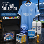 Manchester City FC fan collection display featuring a light blue jersey with Etihad Airways sponsor, a black presentation box with team flags, a framed photo, a blue mug, two white water bottles, a small trophy, and a branded box on a dark marble surface.