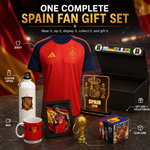 A Spain soccer fan gift set displayed on a dark tabletop with a red-and-navy jersey as the main item, plus a white water bottle, red mug, framed photo, illuminated Spain plaque, small trophy, club cube box, and black gift box. Large text at the top reads 'ONE COMPLETE SPAIN FAN GIFT SET' with callout labels for jersey, custom sipper, gift box + collectibles, mug, and club cube.