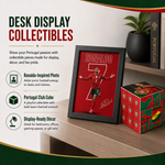 A framed Portugal football collectible featuring Ronaldinho on a red background, displayed on a wooden desk next to a red and green 'Portugal Cube' puzzle block. The image includes promotional text on the left side.