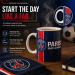 A Paris Saint-Germain ceramic mug with a navy blue body, red and white vertical stripes, and the PSG logo, shown on a wooden desk with coffee steam rising. The scene includes promotional text, a circular inset of the mug handle, a matching PSG coaster, and a soccer ball in the background.