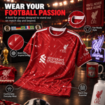 A red Liverpool FC football jersey is displayed on a wooden table with multiple callout graphics highlighting design features. The jersey has white shoulder stripes, a white 'standard chartered' sponsor logo on the chest, and a white 'LFC' crest on the right chest.