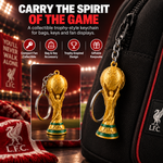 A gold FIFA World Cup trophy keychain shown attached to a black bag, with a smaller inset of the keychain alone. The scene includes Liverpool FC branding and stadium lighting, plus marketing text about carrying the spirit of the game and key features.