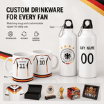 Customizable white German football-themed drinkware set including mugs, water bottles, a jersey print, trophy, box, and framed photo, with text reading 'CUSTOM DRINKWARE FOR EVERY FAN' on a light background.
