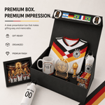 A premium Germany soccer-themed gift box set displayed open on a light beige background. The set includes a black presentation box with German flags on the inside lid, a white soccer jersey with black and red trim, a white mug with the number 11, a clear acrylic trophy cup, a small gold replica trophy, a water bottle, a small box, and a framed picture.