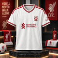 A white Liverpool Football Club home jersey with red trim, featuring the club crest, Standard Chartered sponsor logo, and Exel sports sleeve branding, displayed on a black marble pedestal in a themed fan-zone setting.