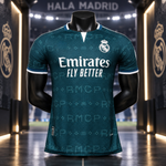 A dark teal Real Madrid soccer jersey displayed on a black mannequin torso in a stadium-themed interior. The jersey features the white Emirates Fly Better sponsor logo on the chest, the Real Madrid crest, and subtle repeating pattern details.
