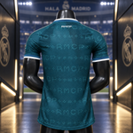 A dark teal Real Madrid soccer jersey with a tonal RMCP monogram pattern, shown from the back on a black mannequin. The jersey features white trim at the collar and sleeve cuffs, and the Real Madrid crest is visible on the background tunnel walls.