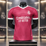 A Real Madrid soccer jersey in dark pink with white accents, displayed on a black mannequin torso. The jersey features the white 'Emirates FLY BETTER' sponsor logo on the chest and the Real Madrid crest on the left chest.